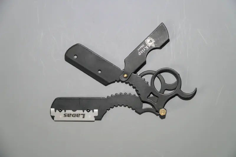 A mini straight razor with swappable blade and finger ring pulled apart to show how the swappable blade feature works
