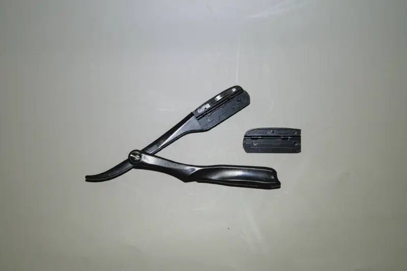 A swappable blade, folding straight razor with the blade compartment open & parts shown
